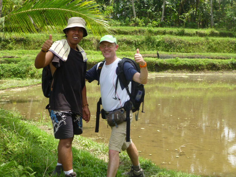 Jalu et un voyageur posant devant une rizière inondée après la récolte